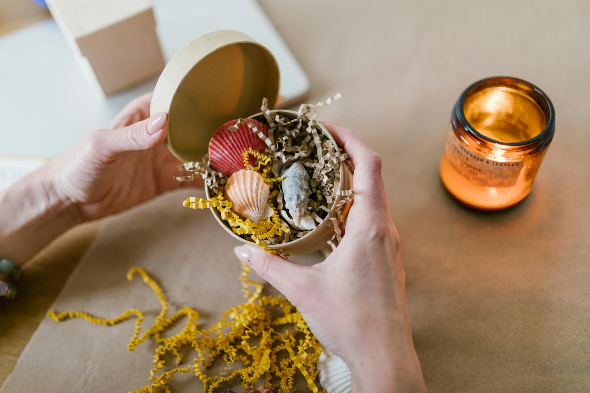 Hand holding a gift box with seashells and a candle creating a cozy atmosphere.